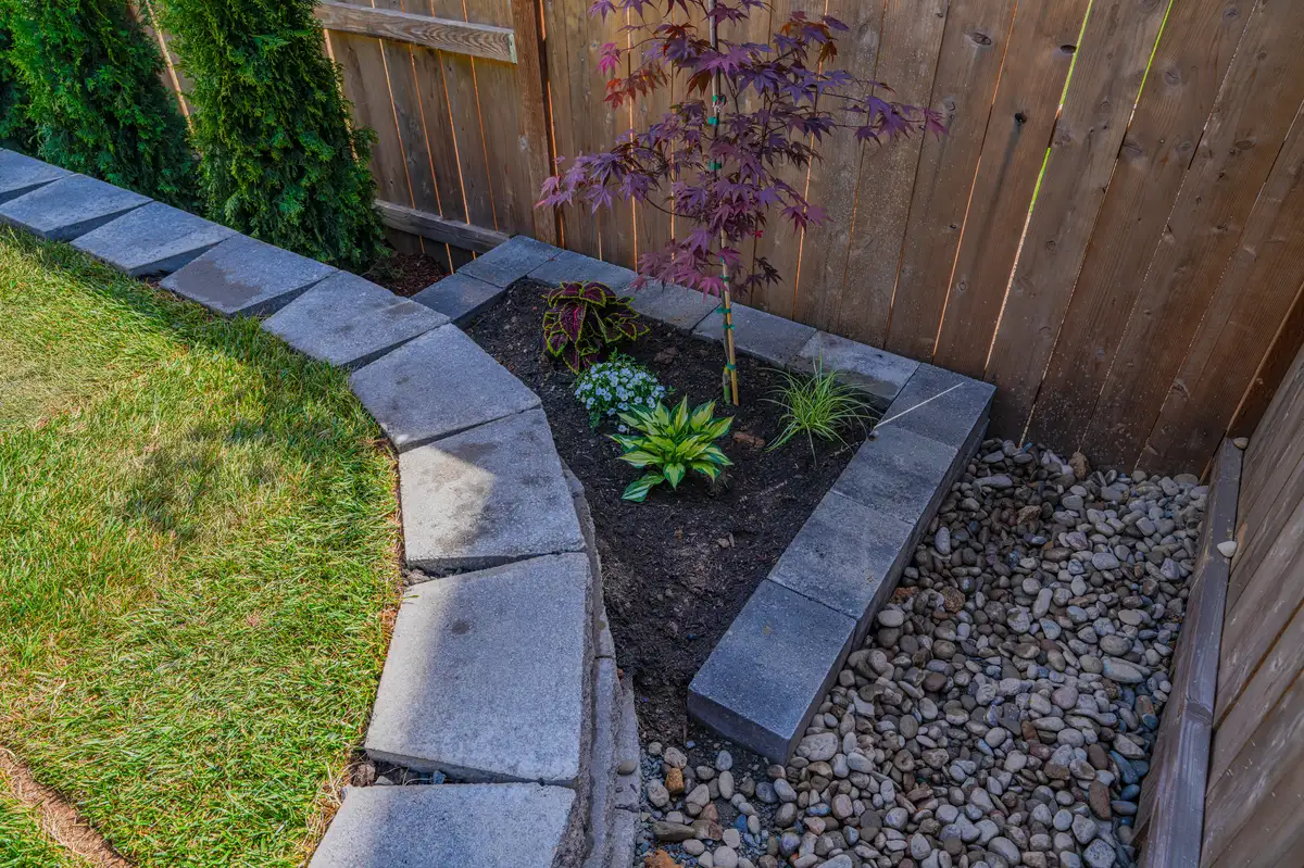 Finished lawn edge, raised planting bed, and river rock drainage detail