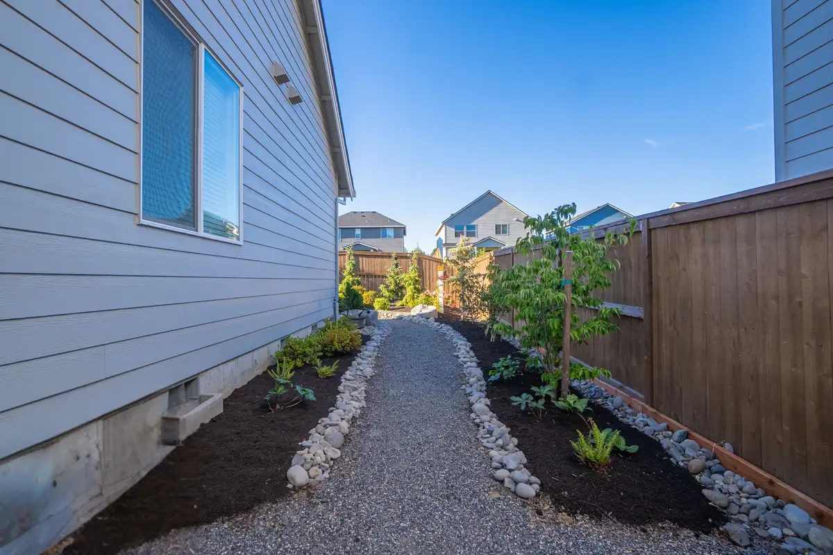 Finished side-yard landscape with a gravel path, river rock edging, and new plantings